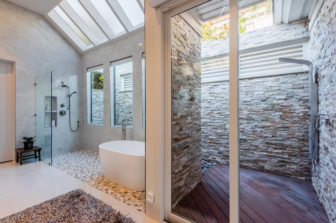 Luxury master bathroom featuring a freestanding white soaking tub, marble-tiled walls, and a large walk-in glass shower.