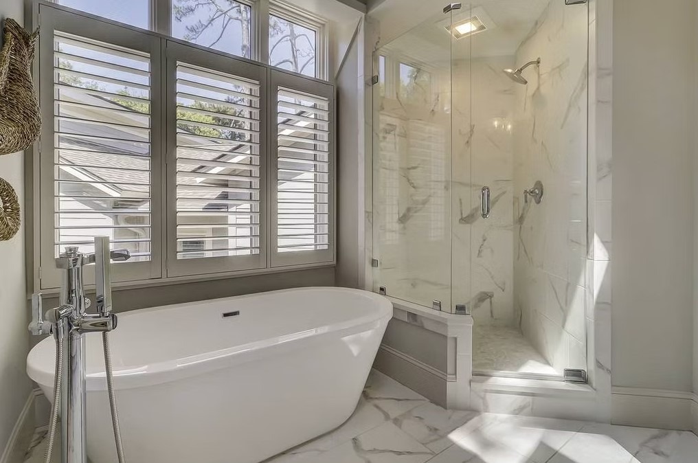 Luxury master bathroom featuring a freestanding white soaking tub, marble-tiled walls, and a large walk-in glass shower.