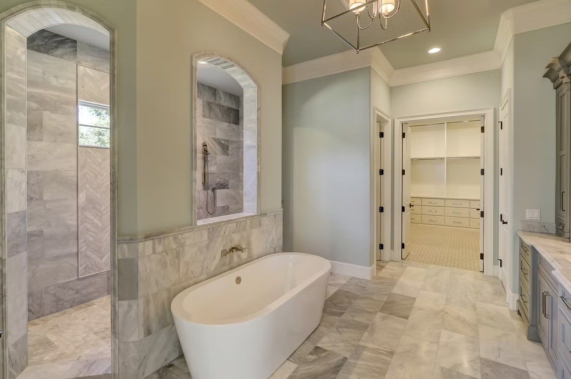 Luxury master bathroom featuring a freestanding white soaking tub, marble-tiled walls, and a large walk-in glass shower.