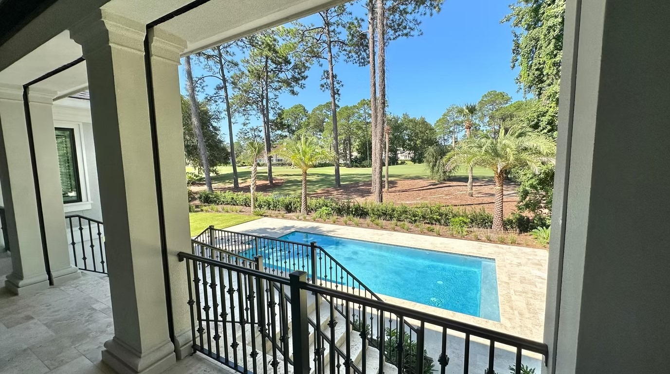 Expansive rear view of a modern luxury estate featuring massive glass windows, a white and charcoal exterior, and a large manicured lawn.