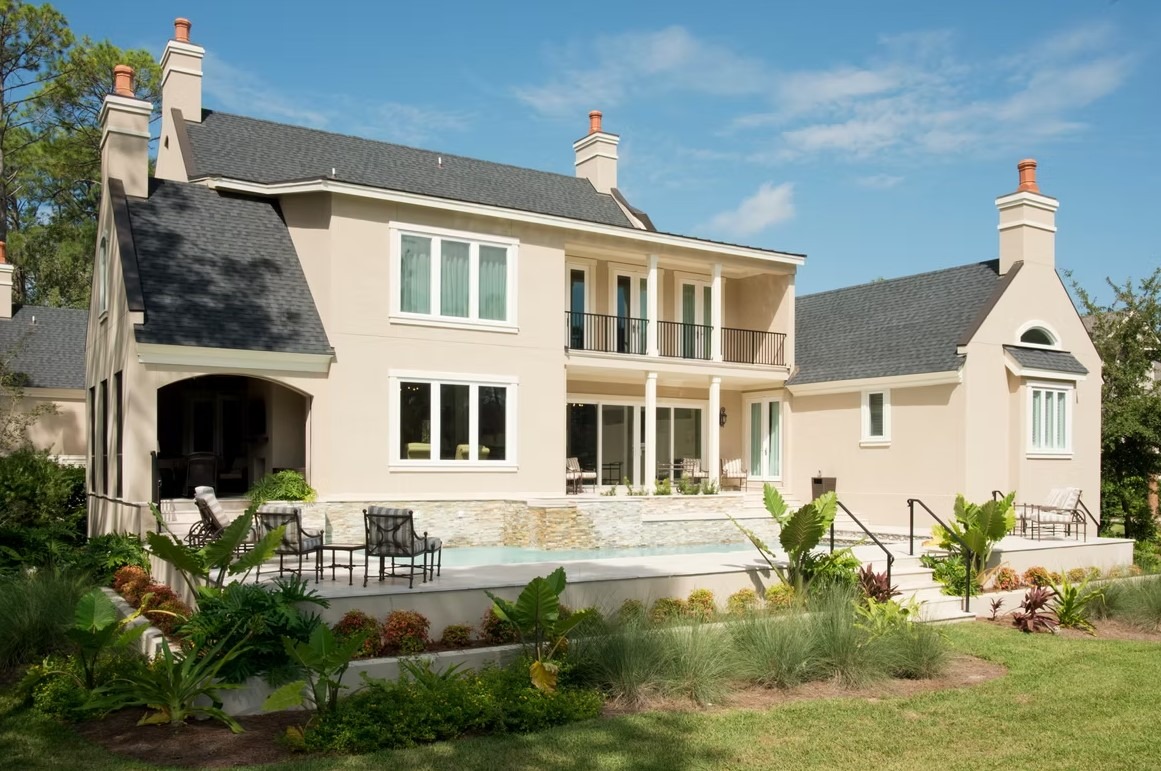 Rear view of a grand modern estate featuring floor-to-ceiling glass windows, a white and charcoal exterior, and a vast manicured lawn.