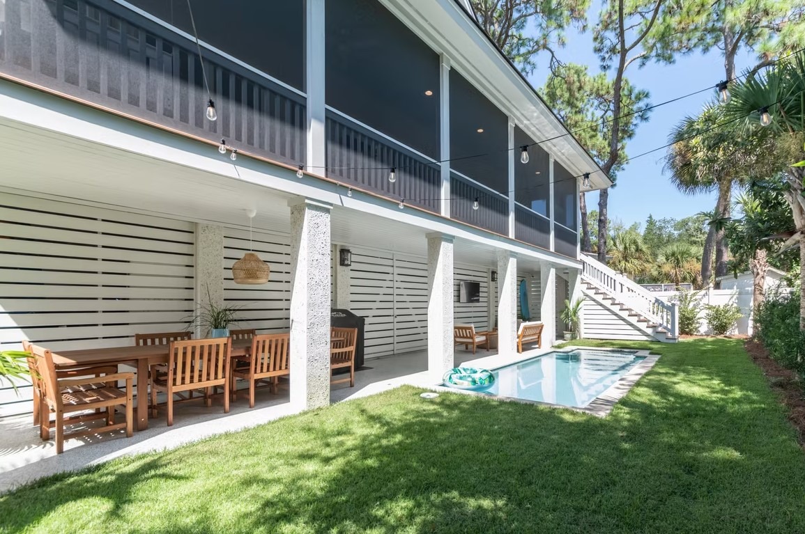 Rear exterior view of a modern luxury mansion featuring massive glass windows, a white and grey facade, and a spacious manicured lawn.