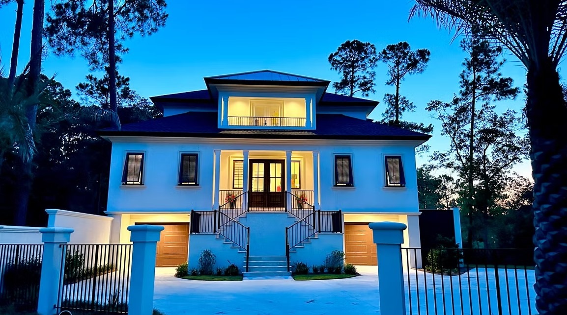 High-angle architectural view of a modern luxury estate’s rear exterior, featuring expansive windows and a large, flat green lawn.