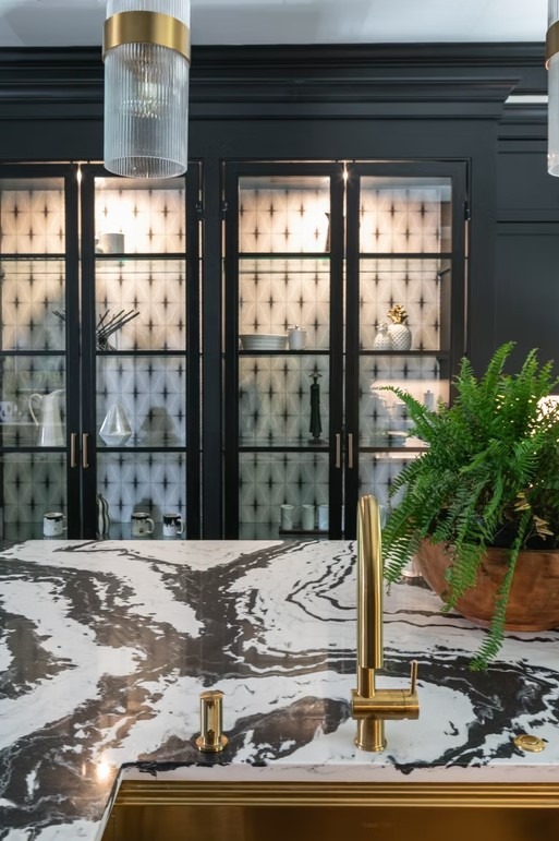 High-end kitchen featuring a large stone-topped island with modern leather bar stools, minimalist cabinetry, and a walk-in butler's pantry in the background.