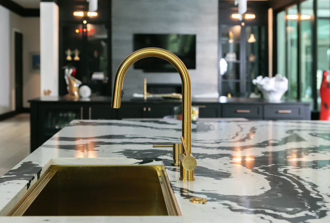 Transitional luxury kitchen featuring a navy blue center island, white shaker cabinets, and gold-finished linear pendant lighting.