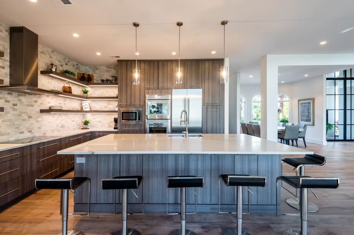 Expansive luxury kitchen with a double-island layout, featuring light marble surfaces, white cabinetry, and transitional pendant lighting.